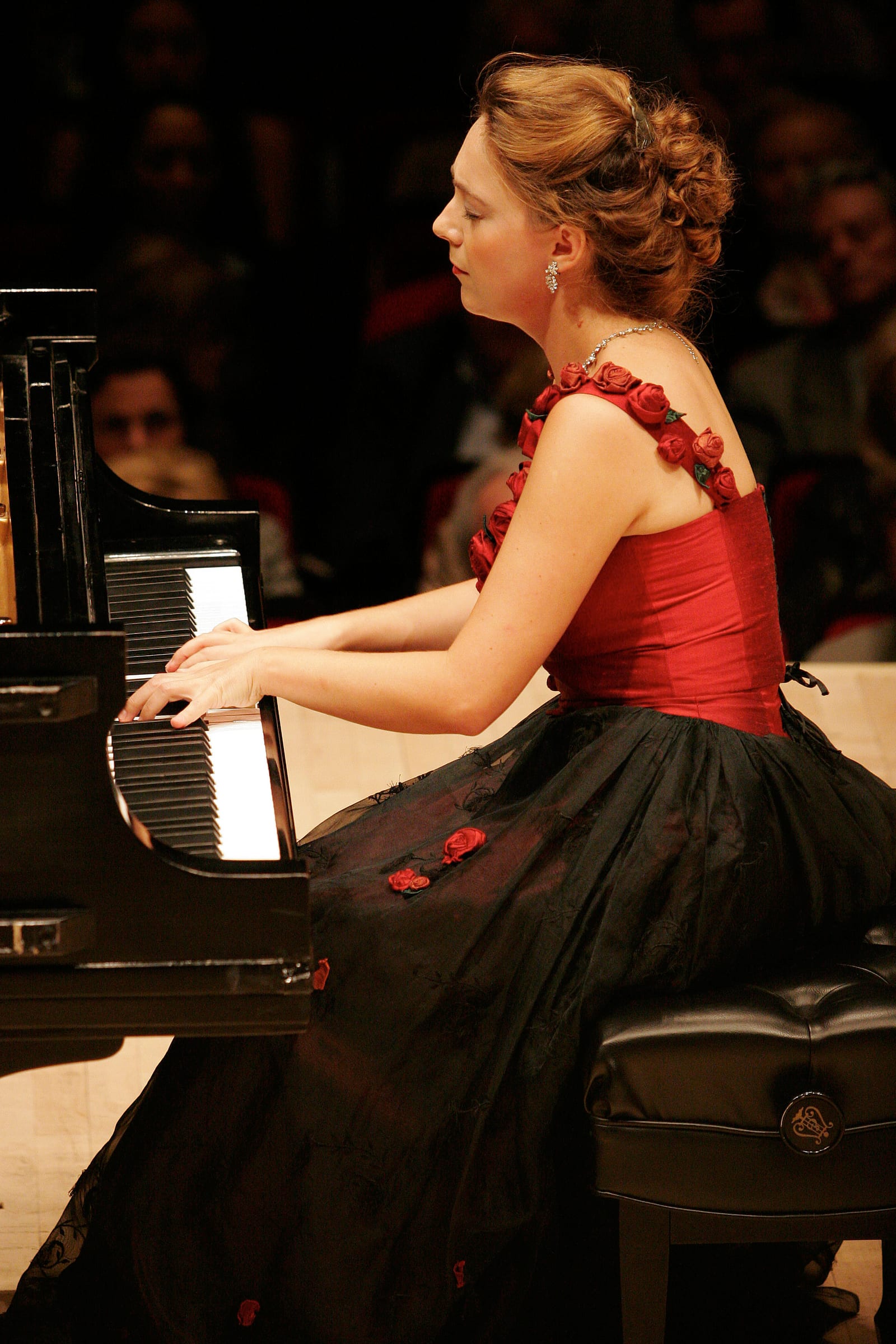 Katya Grineva playing at Carnegie Hall in a red gown with rose straps